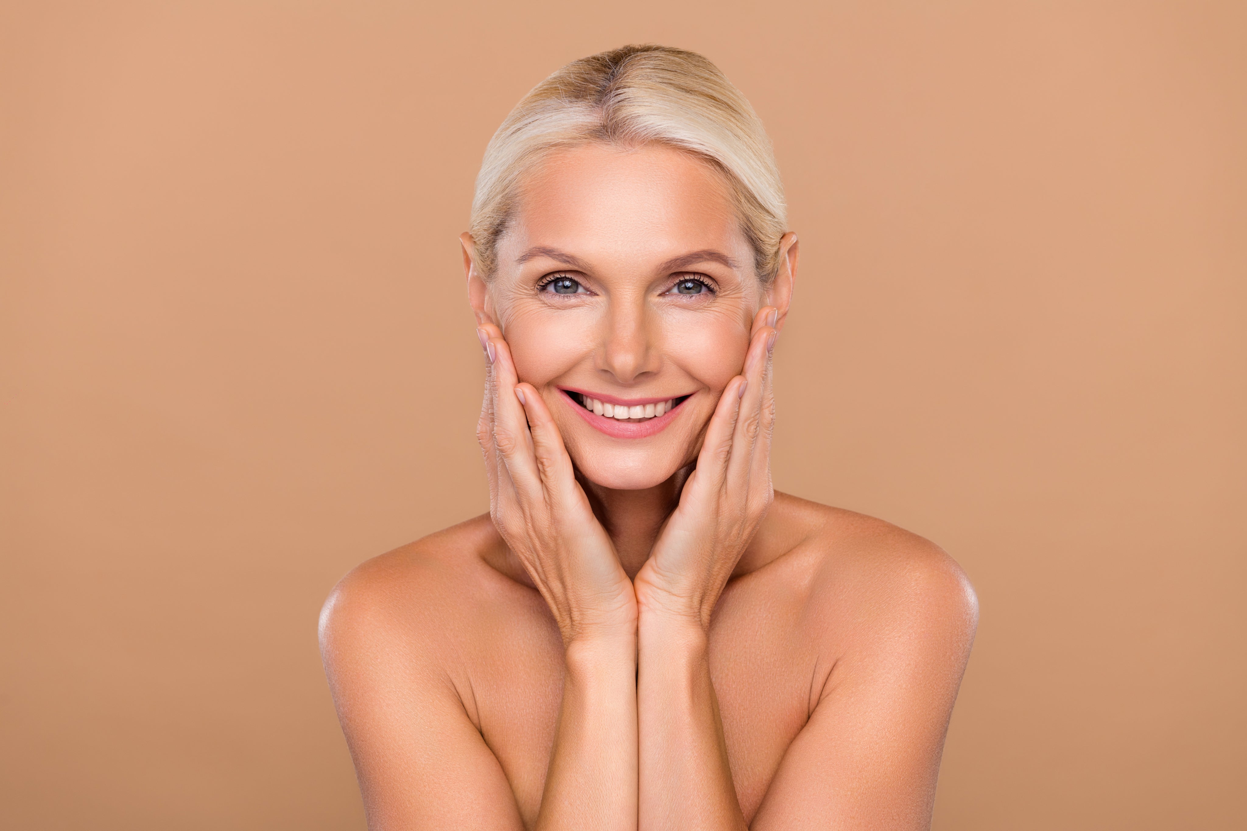 bézs háttér előtt középkorú nő mosolyog, hibátlan bőrrel